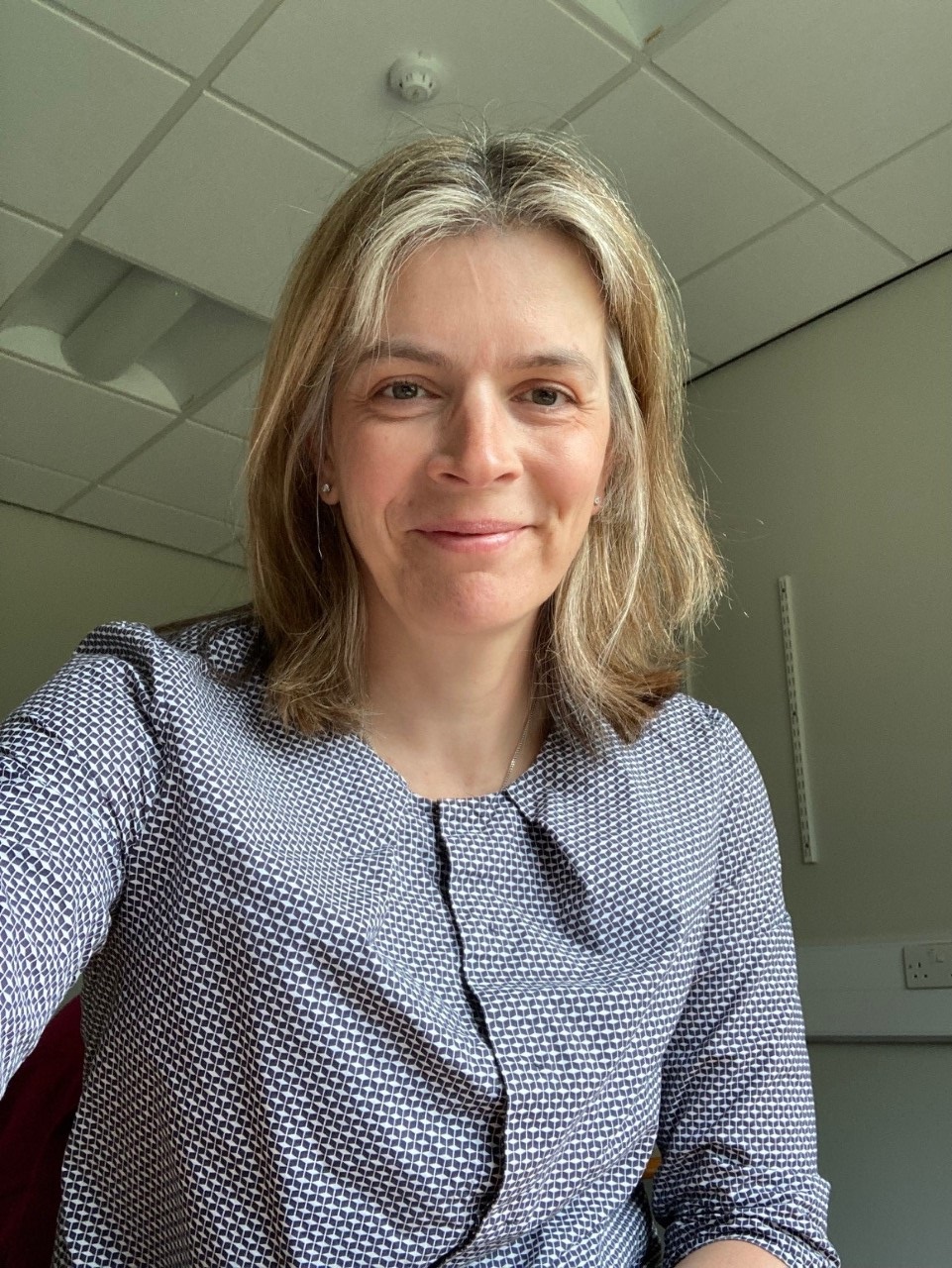 Dr Gow smiling to camera in an office wearing a blue and white checked shirt